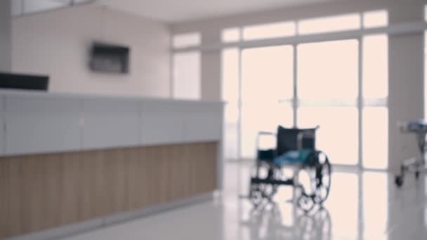 锁定目标 医院或诊所大厅和走廊的背景模糊不清 医护人员的柜台和检查室前面的空轮椅 现场没有人 — 图库视频影像