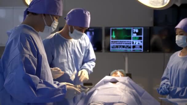 手持ち型ミディアムショット 選択的な焦点 手術を行う医療チーム 医師は手術室で患者の体に外科医を集中させました — ストック動画