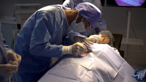 在手术室里 一组专业的外科医生手握近距离拍摄 在麻醉状态下对女性病人进行手术切除 年轻的男性助手和护士移交工具 — 图库视频影像