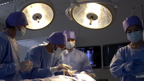 手持ち型の低角度ショット 専門外科医チームは 手術室のベッドの麻酔の下で女性患者に手術切断を行い 若いアシスタントの男性と看護師がツールを介して手術を行います — ストック動画