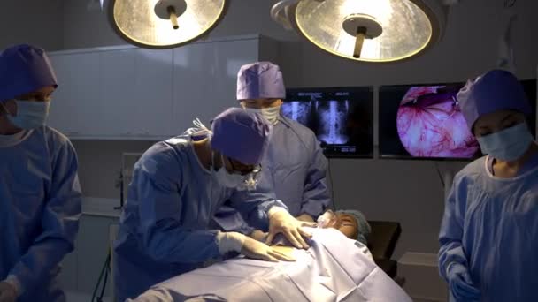 手持式拍摄 专业外科医生小组在手术室对麻醉下的女病人进行手术 医生摘下眼镜 在手术过程中辅助擦拭外科医生脸上的汗珠 — 图库视频影像