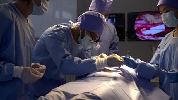 手持式拍摄 专业的外科医生小组在手术结束后进行讨论 女病人在手术室床上麻醉 — 图库视频影像