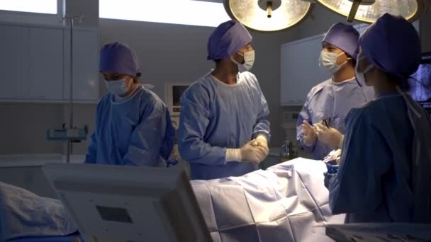 手持式拍摄 专业的外科医生在手术结束后进行手部检查和讨论 手术成功 女病人在手术室床上麻醉 — 图库视频影像