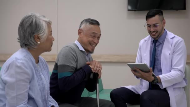 手持ちのショット 若い薬剤師は病院で成熟した患者の男性と彼の妻に薬について説明しながらタブレットを使用します — ストック動画