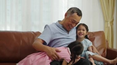 Orta ölçekli, Asyalı emekli adam, oturma odasında iki sevimli torunu tarafından çevrelenmiş saf mutluluğu buluyor. Emeklilik hayatı için mükemmel bir ortam yaratıyor.