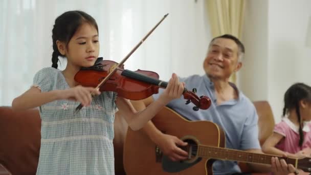 手持锁弹 精选焦点可爱的女孩拉小提琴 高兴的祖父和孙女喜欢在客厅里一起弹奏吉他 小提琴和口琴 — 图库视频影像
