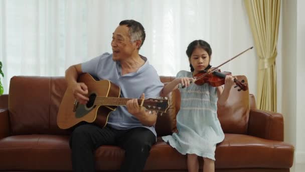 ショットでハンドヘルドズーム アジアの祖父ギターを演奏し ヴァイオリンで歌い 素敵な孫娘の遊び 一緒に音楽を楽しむ 家族の愛の暖かさ — ストック動画