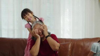 El kamerası görüntüsü orta boy, koltukta oturan neşeli büyükanne oturma odasında tabletle oynayan küçük tatlı bir kız torununla kapalı gözlerle iyi eğlenceler.