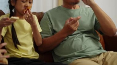 Görüntüler el kamerasıyla çekilmiş, iki Asyalı kardeş ve bir Emeklinin oturma odasında oturması, dedemle torunun evde lezzetli atıştırmalıklar yemeleri.