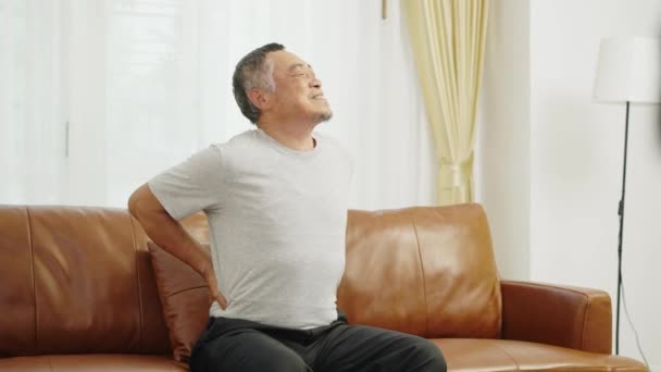 镜头手握中枪 亚洲退休男子坐在客厅沙发上 背痛难忍 他靠自己按摩背缓解背痛 — 图库视频影像