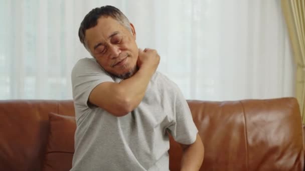 镜头手握中枪 亚洲退休男子坐在客厅沙发上 肩膀酸痛 他自己按摩脖子和肩膀以减轻背痛 — 图库视频影像