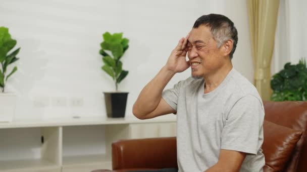 视频手持中枪 亚洲退休男子坐在客厅的沙发上 因头疼而闭上眼睛 他自己按摩两间寺庙以减轻头部疼痛 — 图库视频影像