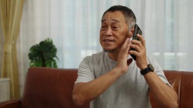 Görüntüler orta ölçekli, Asyalı emekli kalp atışlarını kontrol ediyor ve kalp atışlarını kontrol ediyor. Kalp krizi geçirdikten sonra acil yardım çağırmak için akıllı telefonu kullanıyor.