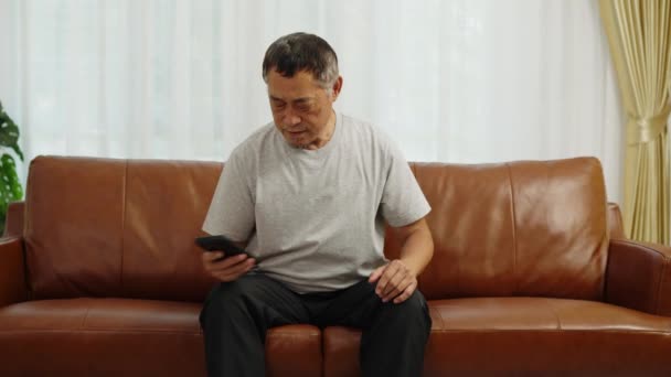 Nagranie Ręczne Średniego Ujęcia Azjata Emeryt Siedzi Kanapie Używając Smartfona — Wideo stockowe