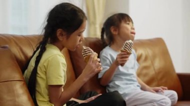 Görüntüler orta boy, iki Asyalı kardeş koltukta oturmuş elinde çikolatalı dondurma külahıyla lezzetli dondurmalar yiyor ve birlikte mutlu mesut başparmağınızı kaldırıyorsunuz.