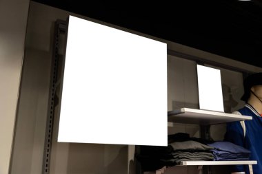 Model boş pankart rafta güzel tişört yığını, reklam, satış indirimi, markalar, özel fiyatlar ve giyim mağazasında promosyon için boş yer olan mankenin yanında duruyor.