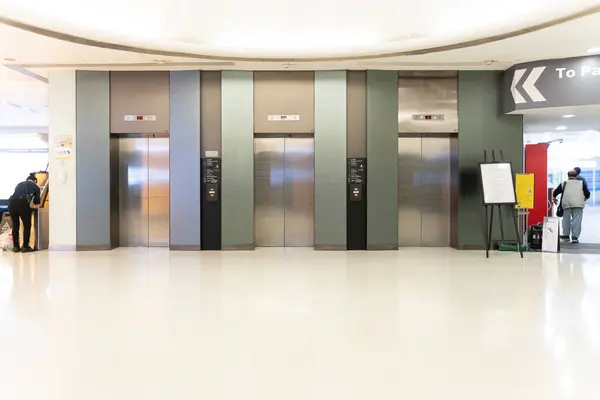 Three passenger Elevators and signboard in lobby of modern building, passengers walking on corridor