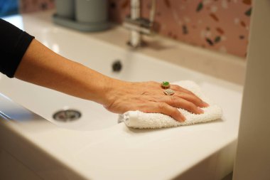 Kesilmiş görüntü, havluyla banyo lavabosunu ve musluğunu temizleyen kadının elini kapat, el jeli şişesini ayarla, evde çalışan hizmetçi.