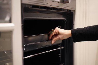 Kırpılmış görüntü, seçici odaklı kadın elleri tepsiyi fırına itiyor, fırını yemek pişirmek ya da mutfakta pişirmek için kullanıyor.