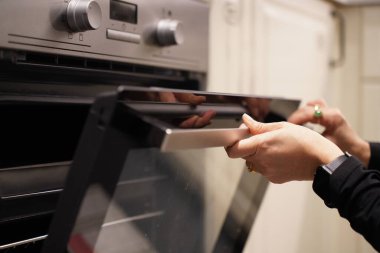 Kesilmiş görüntü, seçici odaklı kadın elleri sıcaklığı ve zamanı ayarlar, fırını yemek pişirmek ya da mutfakta pişirmek için kullanır.