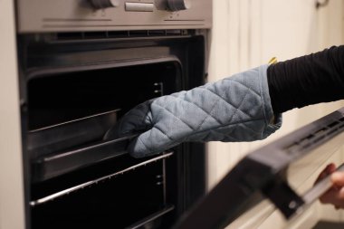 Kırpılmış görüntü, koruyucu eldivenli kadının seçici odak elleri aç ve tepsiyi al, fırını yemek pişirmek ya da mutfakta yemek pişirmek için kullanıyor.