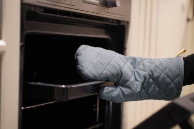 Kırpılmış görüntü, koruyucu eldivenli kadının seçici odak elleri aç ve tepsiyi al, fırını yemek pişirmek ya da mutfakta yemek pişirmek için kullanıyor.