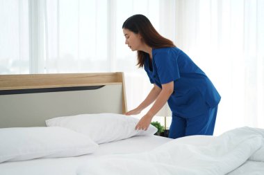 Üniformalı genç bakıcı kadın yatak odasındaki yastıkları ve beyaz yorganı temizliyor ve örtüyordu. Yatma saatine hazırlanıyordu. Yaşlılara bakmak için günlük aktiviteler.