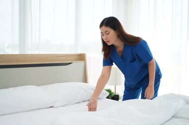 Üniformalı genç bakıcı kadın yatak odasındaki yastıkları ve beyaz yorganı temizliyor ve örtüyordu. Yatma saatine hazırlanıyordu. Yaşlılara bakmak için günlük aktiviteler.