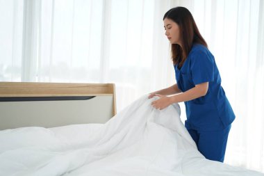 Üniformalı genç bakıcı kadın yatak odasındaki yastıkları ve beyaz yorganı temizliyor ve örtüyordu. Yatma saatine hazırlanıyordu. Yaşlılara bakmak için günlük aktiviteler.