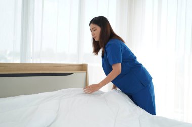 Üniformalı genç bakıcı kadın yatak odasındaki yastıkları ve beyaz yorganı temizliyor ve örtüyordu. Yatma saatine hazırlanıyordu. Yaşlılara bakmak için günlük aktiviteler.