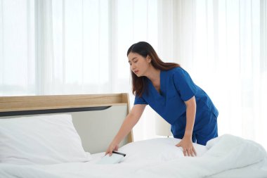 Üniformalı genç bakıcı kadın yatak odasındaki yastıkları ve beyaz yorganı temizliyor ve örtüyordu. Yatma saatine hazırlanıyordu. Yaşlılara bakmak için günlük aktiviteler.