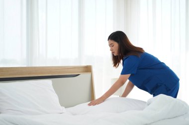 Üniformalı genç bakıcı kadın yatak odasındaki yastıkları ve beyaz yorganı temizliyor ve örtüyordu. Yatma saatine hazırlanıyordu. Yaşlılara bakmak için günlük aktiviteler.