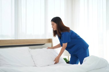 Üniformalı genç bakıcı kadın yatak odasındaki yastıkları ve beyaz yorganı temizliyor ve örtüyordu. Yatma saatine hazırlanıyordu. Yaşlılara bakmak için günlük aktiviteler.