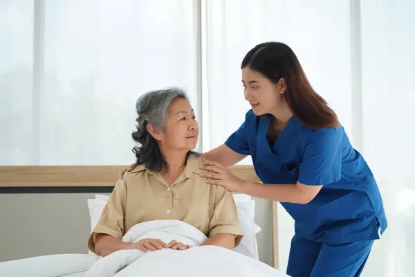 Young Nursing assistant talking and helping senior woman lying down in the bed, Caregiver female Help cover her with a blanket and make sure she sleeps comfortably at home