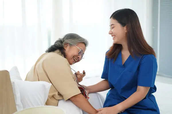 作为一种业余爱好或职业疗法 亚洲的一位老年妇女坐在床上打杂 她教年轻的女性护理人员 她们在家里或疗养院一起玩得很开心 图库照片
