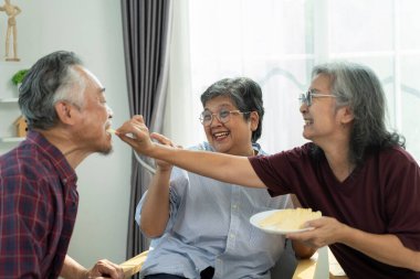 Seçici odak, iki Asyalı son sınıf öğrencisi erkek arkadaşına patates cipsi yedirip birlikte eğlenerek gülüyorlar, emeklilik grubu toplanıyor ve oturma odasında vakit geçiriyorlar.