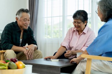 Asyalı son sınıf öğrencisiyle iki bayan arkadaş iskambil kağıdıyla eğleniyorlardı, mutlu bir şekilde konuşup gülüyorlardı. Emeklilik Grup toplantısı mutlu bir şekilde evde yapılacak.