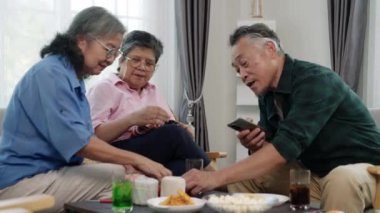 Emekliliğin tadını çıkaran Asyalı arkadaşların el kamerasıyla çekilmiş videosu. İki kadın örgü örerken, bir erkek telefonunu rahat bir oturma odasında atıştırmalık ve içeceklerle kontrol ediyor, arkadaşlığı ve modern teknoloji kullanımını ön plana çıkarıyor..