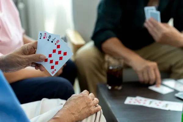 stock image Selective focus, close-up showing her hands holding playing cards, revealing a lucky hand. The blurred background features a person. Senior friends enjoy a card game in living room