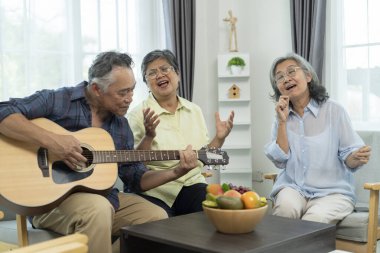 Üç Asyalı mutlu yaşlı arkadaş müzik ve arkadaşlığın tadını çıkarıyor, olgun bir adam akustik gitar tıngırdatırken, bayan arkadaşlar parlak bir oturma odasında şarkı söylüyorlar..