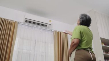 El kamerasıyla çekilen görüntüler, önlüklü yorgun bir hizmetçi evi temizliyor. Sıcak hissettiği için oturma odasındaki klimayı açar ve serinler..
