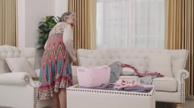 Renkli kıyafetli bir ev kadınının dağınık giysileri temizleyerek dağınık oturma odanızı düzenleyin. Uzayı etkin bir şekilde düzenle