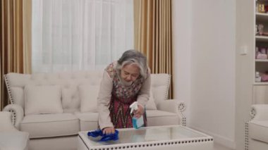Ev hanımı renkli bir elbise içinde cam bir sehpayı temizlerken sırt ağrısı çekiyor. Angarya işlerden bitkin bir şekilde kanepede oturuyor..