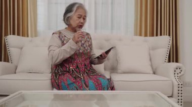 El kamerası görüntüsü, renkli elbiseli hizmetçi bir bardak su tutuyor ve bir tablet kullanıyor oturma odasındaki kanepede dinleniyor..