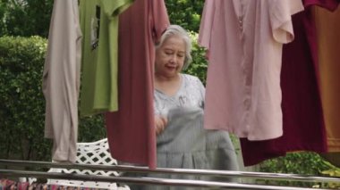 Görüntüler orta ölçekli, Asyalı son sınıf öğrencisi çamaşırları çamaşır ipine astı güneş ışığıyla, yaşlı bir kadın rutin olarak çalışıyor ve evde tekstil temizliği yapıyor.