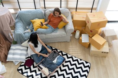 Yüksek açılı manzara, seyahat etmeye hazırlanan iki genç Asyalı kadın akıllı telefon ve selfie ile birlikte oturma odasında dinleniyorlar.