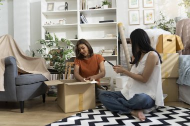 Konforlu Salon 'da taşınma kutularını açan iki Asyalı kadın akıllı telefondan listeyi kontrol ediyor. Mutlulukla konuşuyorlar.