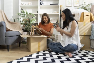 Konforlu Salon 'da taşınma kutularını açan iki Asyalı kadın akıllı telefondan listeyi kontrol ediyor. Mutlulukla konuşuyorlar.