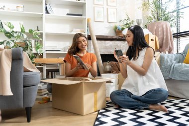Konforlu Salon 'da taşınma kutularını açan iki Asyalı kadın akıllı telefondan listeyi kontrol ediyor. Mutlulukla konuşuyorlar.