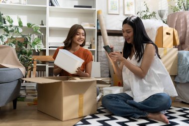 Konforlu Salon 'da taşınma kutularını açan iki Asyalı kadın akıllı telefondan listeyi kontrol ediyor. Mutlulukla konuşuyorlar.